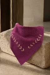 Bandana triangular de cuero color bordó, con detalle de tachas metálicas doradas en todo el borde. Diseño versátil para usar como accesorio de cuello.