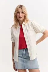 Camisa de manga corta abullonada color blanco marfil, con cuello clásico y cierre frontal de botones.