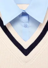 Jersey de punto grueso en color crema con cuello en V y detalles en contraste azul marino. Presenta un diseño recto de manga larga con efecto de camisa superpuesta en color celeste.