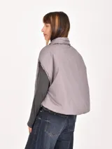 Chaleco puffer corto de color gris, con cuello camisero y cierre frontal oculto. Presenta un diseño holgado y sin mangas.