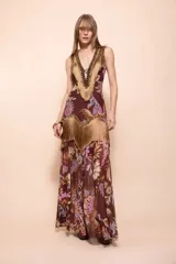 Vestido largo sin mangas de color marrón con estampado paisley y floral en tonos rosados, celestes y beige. Presenta un pronunciado escote en V con detalles de flecos dorados, pedrería y abalorios.