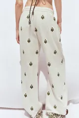 Pantalón color crema de tiro medio con cintura elástica ajustable y bolsillos delanteros. Presenta bordados florales en negro y corte ancho.