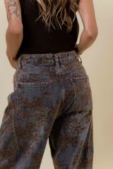 Jean de corte wide leg con estampado floral en tonos tierra sobre base de denim gris oscuro. Presenta tiro medio-alto, bolsillos traseros funcionales y costuras reforzadas.