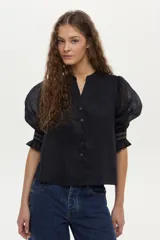Blusa color tostado confeccionada en lino, con mangas abullonadas de ramie y detalles de bordado en punto smock en los puños.