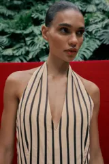 Vestido midi de corte globo con estampado de rayas verticales, cuello halter anudado, escote en pico y espalda descubierta. Presenta bajo abullonado con elástico interior y cierre lateral con cremallera oculta.