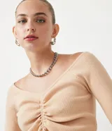 Blusa cropped de punto acanalado color beige, con escote ombro a ombro, manga larga y cordón ajustable con lazo.