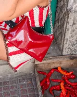 Cartera tipo media luna de cuero natural color marrón, con cierre superior y correa de cadena metálica plateada. Presenta el logo de la marca grabado en el frente.