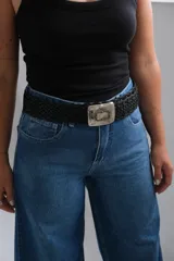 Cinto de cuero trenzado color negro con hebilla metálica rectangular de estilo artesanal, que presenta un detalle central de piedra clara engarzada.