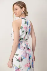 Vestido midi de gasa blanca con estampado floral en tonos rosados, azules y verdes. Presenta escote cruzado, espalda estilo halter, detalle de volados en la falda y corte irregular.