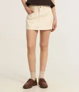 Short pollera de sarga color beige, con diseño de tiro medio, trabillas en la cintura, bolsillos laterales y cierre frontal con botón y cremallera.