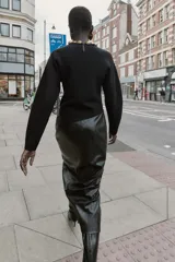 Jersey negro de cuello redondo con aplicación de bolas metálicas doradas, manga larga y bajo asimétrico. Cierre en la espalda con abertura y botón.