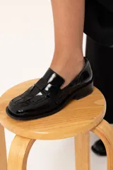 Mocasín de cuero charol negro con diseño enrejillado en la capellada, horma cuadrada y taco bajo.