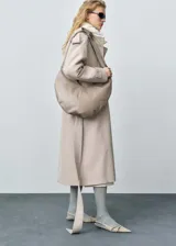 Trench coat de corte oversize en color beige, con cuello de solapa, cierre frontal, cinturón ajustable a la cintura, trabillas en hombros y puños con detalle de botón.