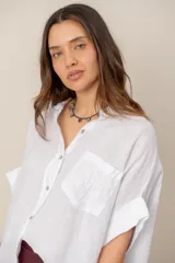 Camisa de lino blanca de manga corta, corte holgado, con cuello camisero, cierre frontal con botones y un bolsillo en el pecho con detalle bordado.