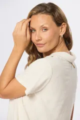 Camisa lisa de lino color beige, de manga corta, con cuello camisero, bolsillo ojal en el pecho y cierre frontal con botones.