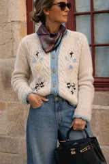 Cardigan de lana merino color marfil, con bordados florales artesanales, trenzas y rombos calados en el frente. Posee cierre frontal con botones vintage dorados y terminaciones en crochet celeste en cuello, puños, ruedo y tira de botones.