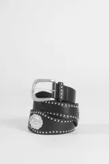 Cinturón de cuero vegano negro con diseño de estilo western, decorado con tachas metálicas plateadas a lo largo de toda la pieza y apliques de medallas ovaladas grabadas.