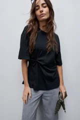 Remera de manga corta color blanco con cuello redondo y detalle de frunce lateral que aporta movimiento y una silueta entallada.