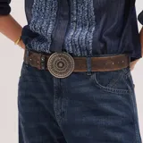 Cinturón de cuero marrón con remaches en tonos plata y oro colocados de forma alternada, y una hebilla circular grande de metal envejecido estilo plata vieja.