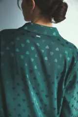 Pijama de dos piezas compuesto por camisa de manga larga con cuello camisero y botones frontales, y pantalón de corte recto y holgado con cintura elástica y cordón de ajuste. Presenta un diseño estampado con pequeños corazones en tono sobre tono.