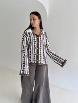 Camisa blanca de manga larga con delicados bordados florales verticales y detalles de encaje. Presenta cuello clásico, cierre frontal con botones y terminaciones festoneadas en los puños y el ruedo.