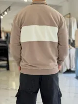Hoodie de corte clásico con medio cierre y cuello alto, en color marrón con una franja horizontal blanca en el pecho que incluye el logo estampado en negro. Presenta además un pequeño bordado en el hombro izquierdo y puños y cintura elastizados de rib.