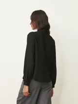 Camisa de manga larga en color blanco, con cuello mao y detalle de volados sutiles en el borde. Presenta cierre frontal oculto con botones y puños con volados.