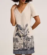 Vestido corto t-shirt de Marfinno confeccionado en viscolino color beige, con escote en V, mangas cortas y estampa en la parte inferior con motivos arquitectónicos y de palmeras en azul marino.