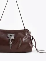 Bandolera de cuero vacuno color marrón con acabado brillante. Presenta un diseño estructurado con herraje metálico tipo candado y llave colgante en el frente, además de detalles de tiras laterales. Incluye correa de hombro y cierre superior.