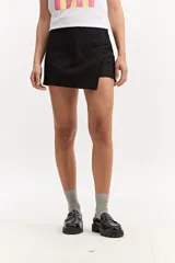 Short pollera sastrero negro con frente cruzado asimétrico y líneas limpias, combinando la estética de una minifalda con la practicidad de un short.