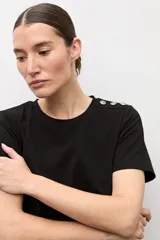 Remera blanca de manga corta con detalle de botones metálicos en el hombro, cuello redondo y corte clásico.