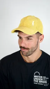 Gorra tipo baseball confeccionada en pana color amarillo, con logo bordado en blanco en el panel frontal y visera curva.