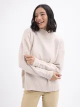 Buzo de punto color beige, con cuello alto y mangas largas con puños acanalados.