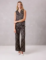 Conjunto de dos piezas compuesto por una blusa sin mangas con cuello solapa y escote en V con botones frontales, y un pantalón de tiro alto con pierna ancha y bolsillos laterales. Ambas prendas están confeccionadas en satén con un estampado floral sobre fondo oscuro.