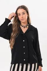 Camisa de manga larga color negro, con cuello camisero, cierre frontal con botones y detalle de volados en la cartera y los puños.