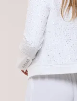 Chaqueta corta confeccionada en tejido bouclé texturizado de color blanco con sutiles lentejuelas. Presenta escote redondo, diseño abierto al frente, bolsillos frontales con solapa y mangas largas con puños de tela lisa.