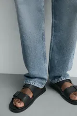 Sandalia negra con dos tiras anchas ajustables mediante hebillas cuadradas. Presenta una plantilla anatómica y suela plana a tono.