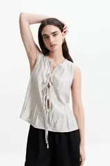 Blusa sin mangas color gris claro con textura rayada vertical y lazo ajustable en el escote.