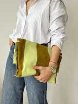 Cartera tipo sobre de cuero y gamuza, con diseño de franjas verticales en tonos verde y marrón, y cierre superior con cordones y borlas colgantes.