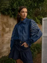 Camisa celeste de denim con bordado de hojas en las mangas, cuello con volados y botones de flor.