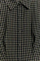 Camisa de cuello solapa y manga corta con pliegues en los hombros. Presenta un diseño de estampado a cuadros y cierre frontal con botones.