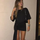 Vestido corto negro con hombreras, diseño holgado en la parte superior y falda ajustada con detalle drapeado y lazo lateral con anilla.