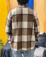 Sobrecamisa de paño con diseño de cuadros grandes en tonos marrón y beige. Presenta cuello clásico, cierre frontal con botones, mangas largas con puños abotonados y dos bolsillos frontales con solapa.