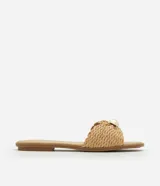 Sandalia plana de color beige con tira ancha confeccionada en rafia trenzada con diseño de nudo. Presenta un detalle decorativo de esfera perlada en el centro, punta redondeada y suela fina de 1 cm.