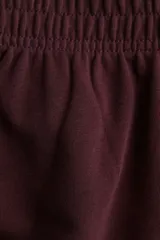 Pantalón deportivo color borgoña, de corte ancho y largo cropped, con cintura elástica.