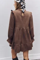 Vestido corto de gamuza color marrón, con diseño de corte evasé, volados en los hombros y mangas largas con puños elásticos fruncidos. Presenta un cuello alto y una falda con un volado en el ruedo.