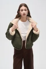 Campera puffer de poliamida color verde militar, con interior y detalles en corderito color crema. Presenta cuello alto, cierre frontal con botones a presión y mangas largas.