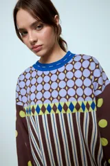 Sweater de punto con diseño geométrico y a rayas, de corte holgado y manga larga. Presenta un patrón combinado de lunares en las mangas, rombos en la parte superior y rayas verticales en el cuerpo.