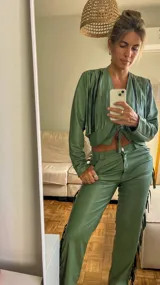 Campera corta verde con flecos negros en la parte superior y cierre frontal con lazo.