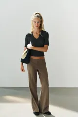 Pantalón de tiro bajo color marrón, con bolsillos frontales, falsos bolsillos traseros de vivo y cierre delantero con cremallera y gancho metálico.